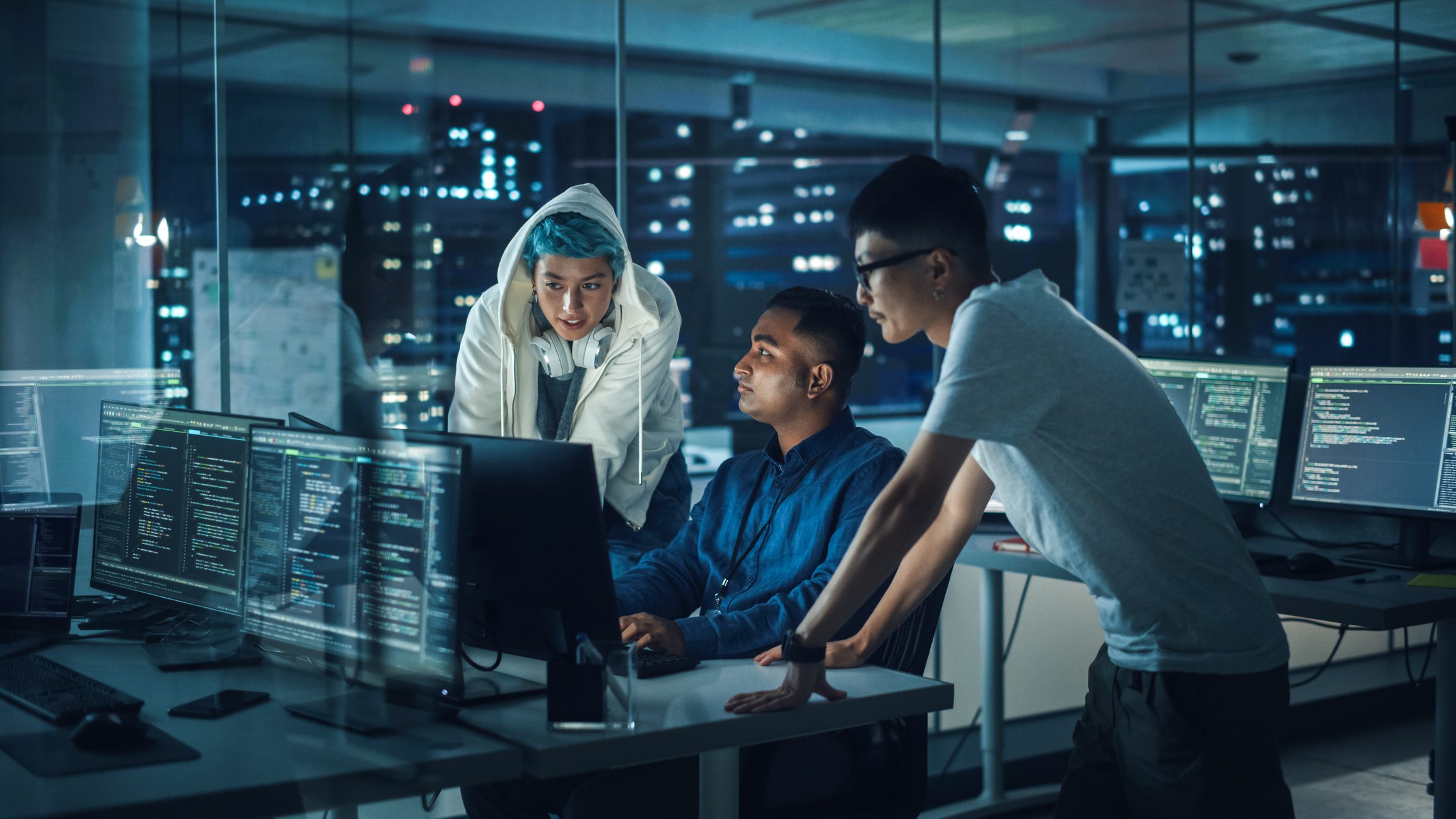Three people working at computers in office.